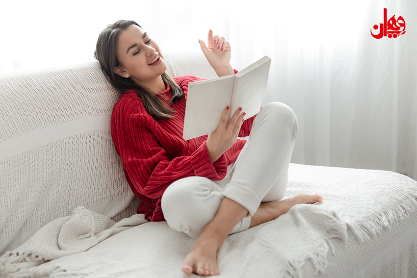 Young woman in a red sweater on the couch at home with a book in her hands.